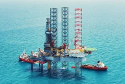 An oil and gas drilling platform out on the water with boats surrounding it